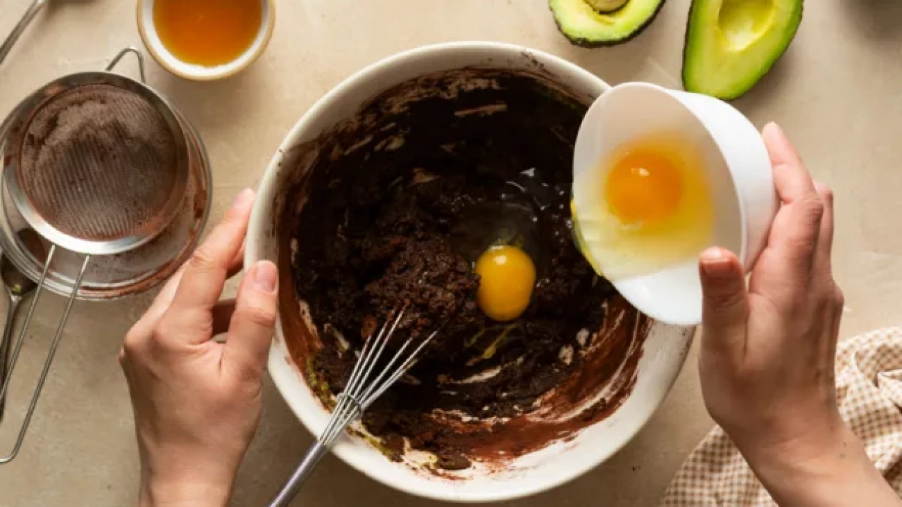 person-pouring-egg-into-avocado-brownie-batter